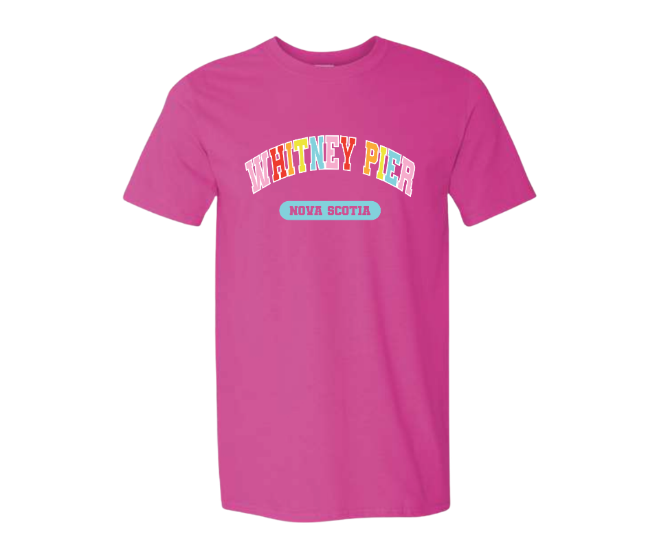 A bright pink short-sleeve t-shirt with a graphic on the chest reading 'WHITNEY PIER' in multicolored letters and a light blue oval below that says 'NOVA SCOTIA'.