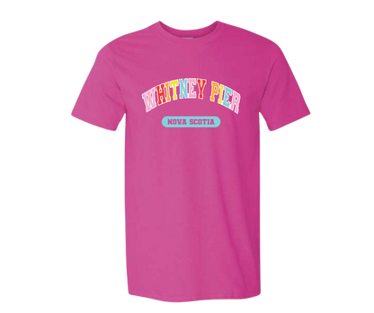 A bright pink short-sleeve t-shirt with a graphic on the chest reading 'WHITNEY PIER' in multicolored letters and a light blue oval below that says 'NOVA SCOTIA'.