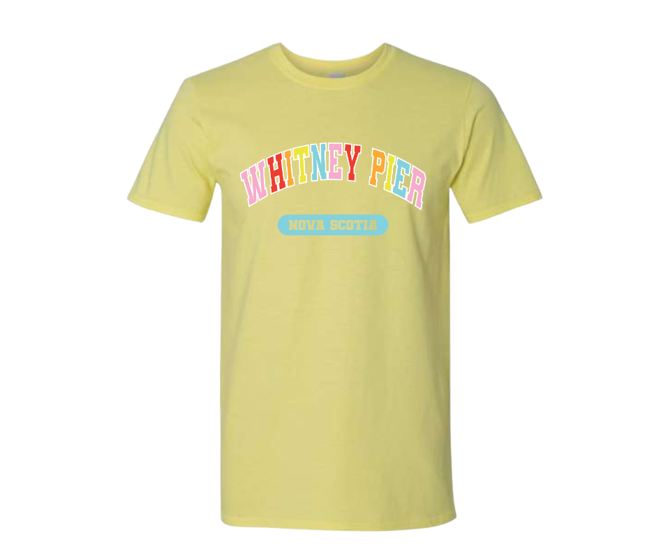 A pale yellow short-sleeve t-shirt with 'WHITNEY PIER' printed in colourful bubble letters and a light blue 'NOVA SCOTIA' graphic on the front, displayed against a solid white background.